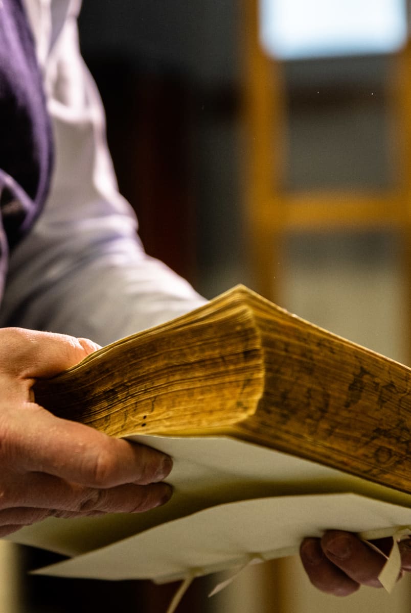 Kuvassa kirjansitoja Lappalainen pitää vanhaa kirjaa kädessään, jossa on satoja sivuja.