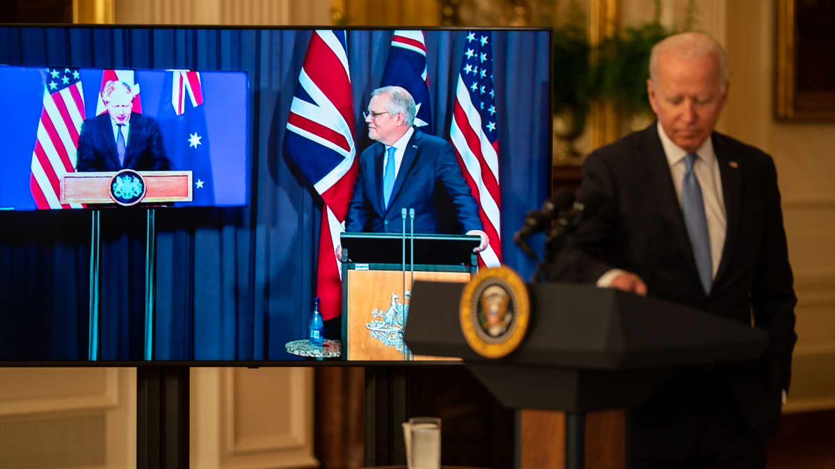 Joe Biden on puhujanpallilla, taustalla Scott Morrison ja Boris Johnson osallistuvat ruuduilla etäyhteyden kautta tilaisuuteen. 