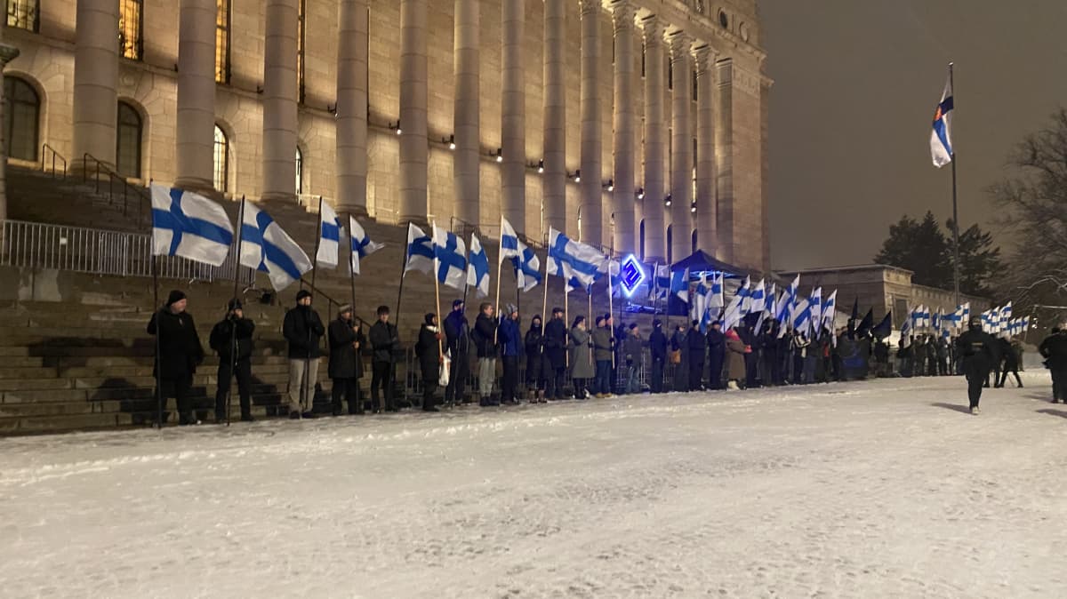 Suomi herää -mielenosoitus on kokoontunut riviin Eduskuntatalon eteen. Suomen lippuja näkyy kuvassa.