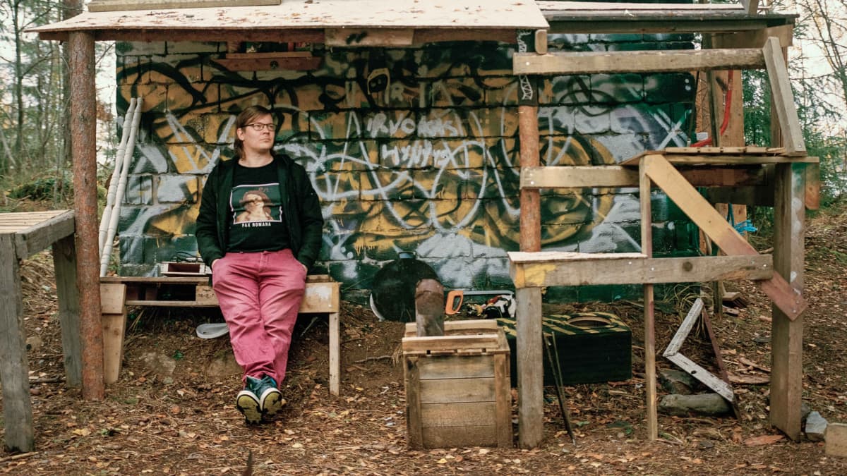 Mies nojaa graffiteilla maalattuun pieneen rakennukseen metsässä.