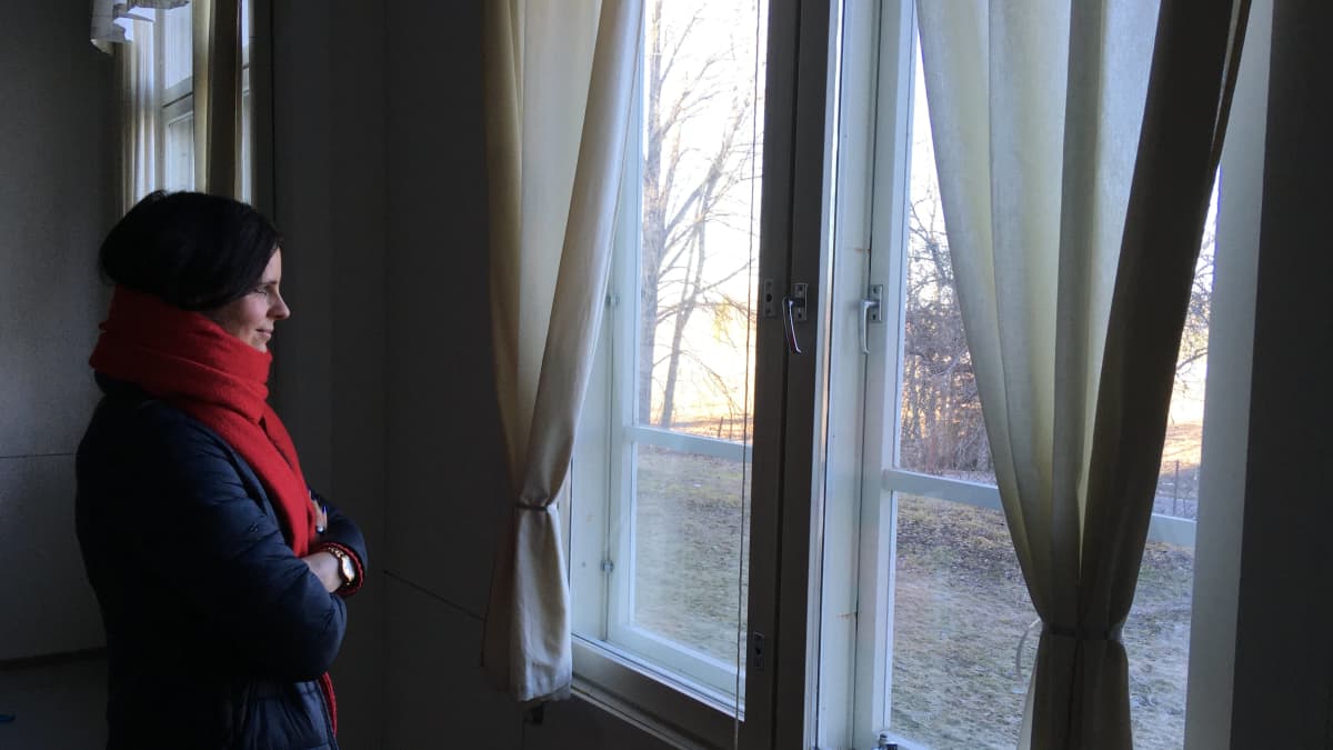 Punaiseen kaulahuiviin kietoutunut nainen katsoo ulos ikkunasta