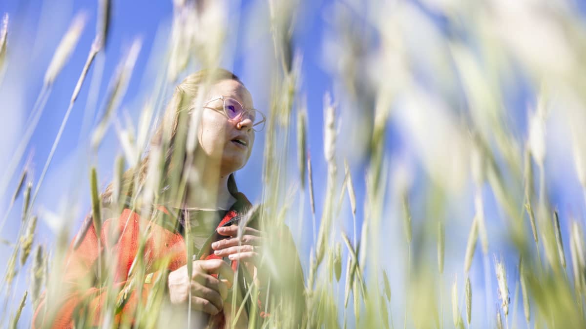 Eliisa Malin seisoo ruispellossa ja katselee eteenpäin. Etualalla rukiita.