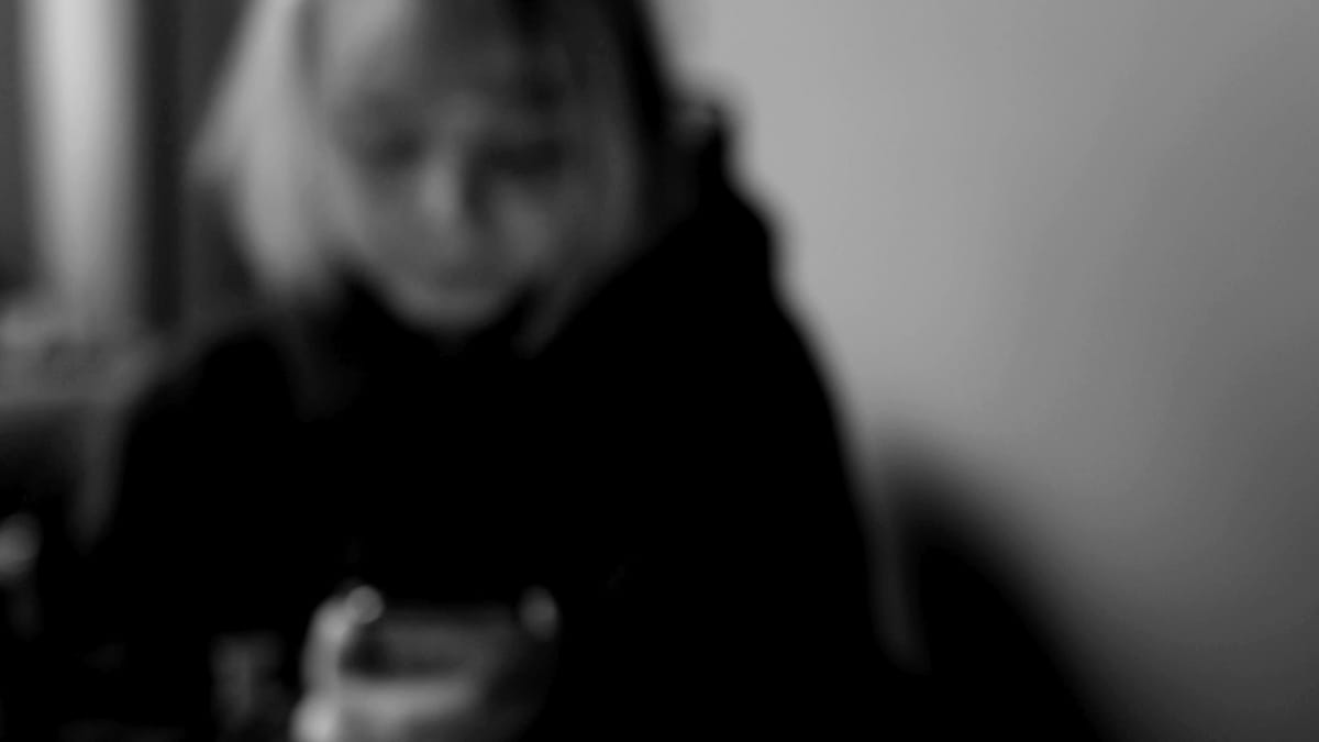 Någon anonym tittar ner på sin telefon. Bilder är svartvit och blurrad.
