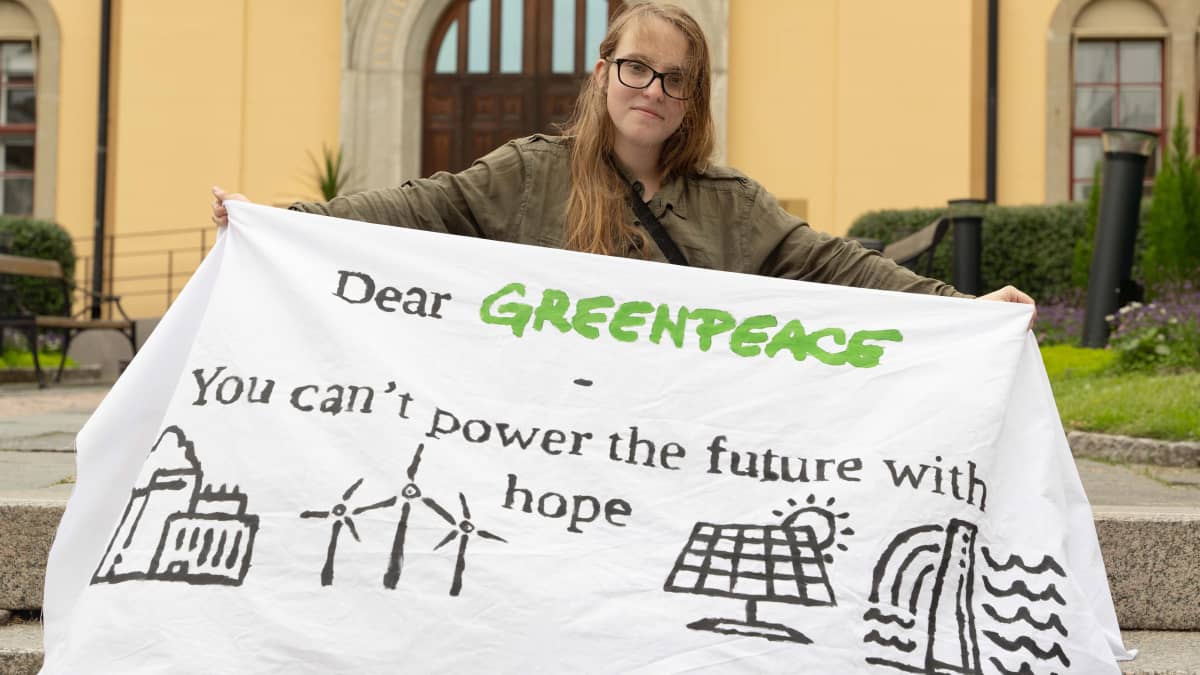 Ruotsalainen Ia Aanstoot pitää kädessään lakanaa, jossa on kuvia aurinko-, tuuli- ja vesivoimaloista ja teksti Dear Greenpeace, you can't power the future with hope.