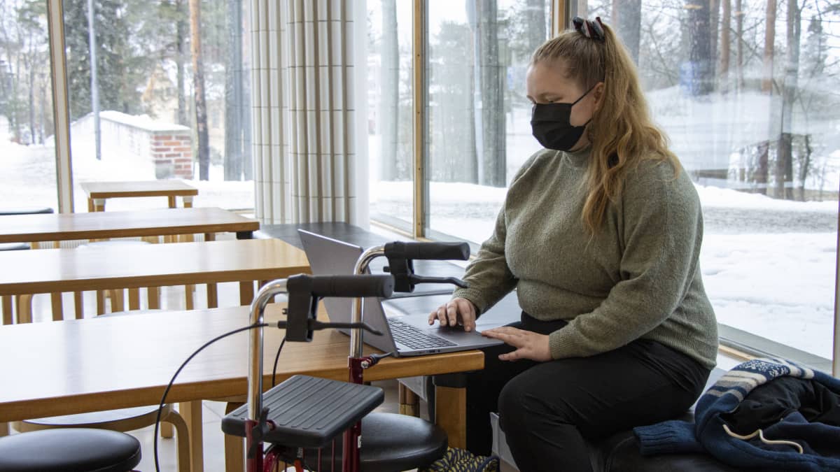 Marja Puustinen istuu yliopiston aulassa ja selaa tietokonetta. 