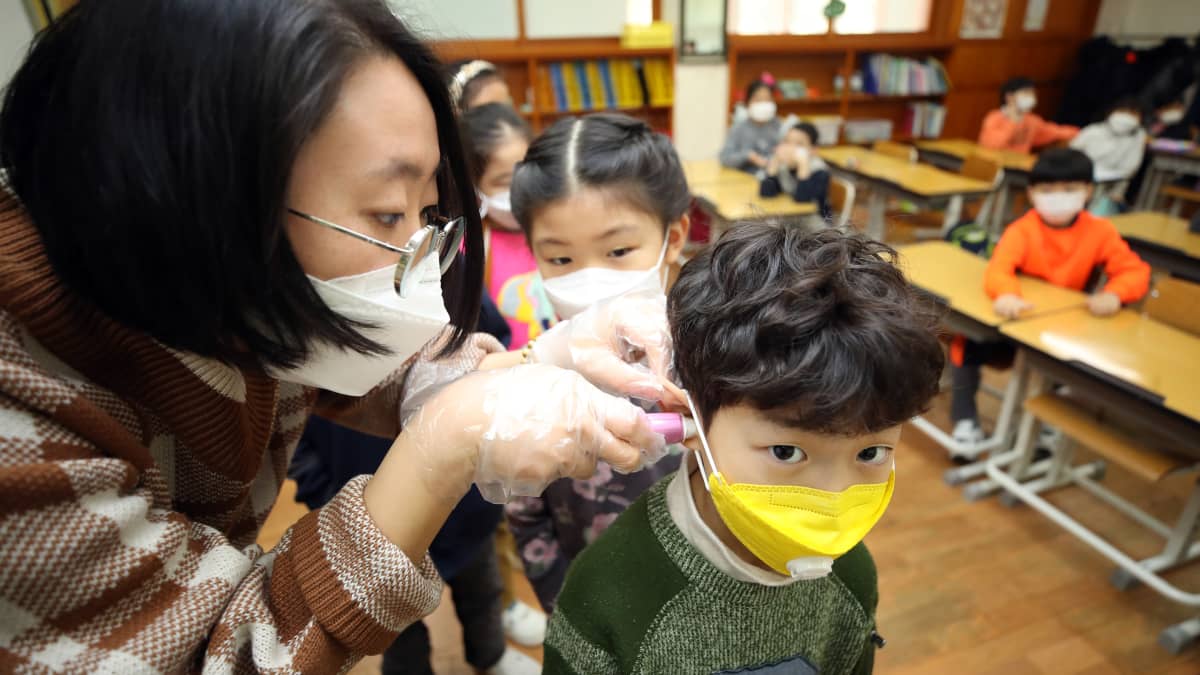 Opettaja mittaa hengityssuojaimeen pukeutuneelta oppilaalta kuumeen Seoulissa Etelä-Koreassa 30. tammikuuta 2020.