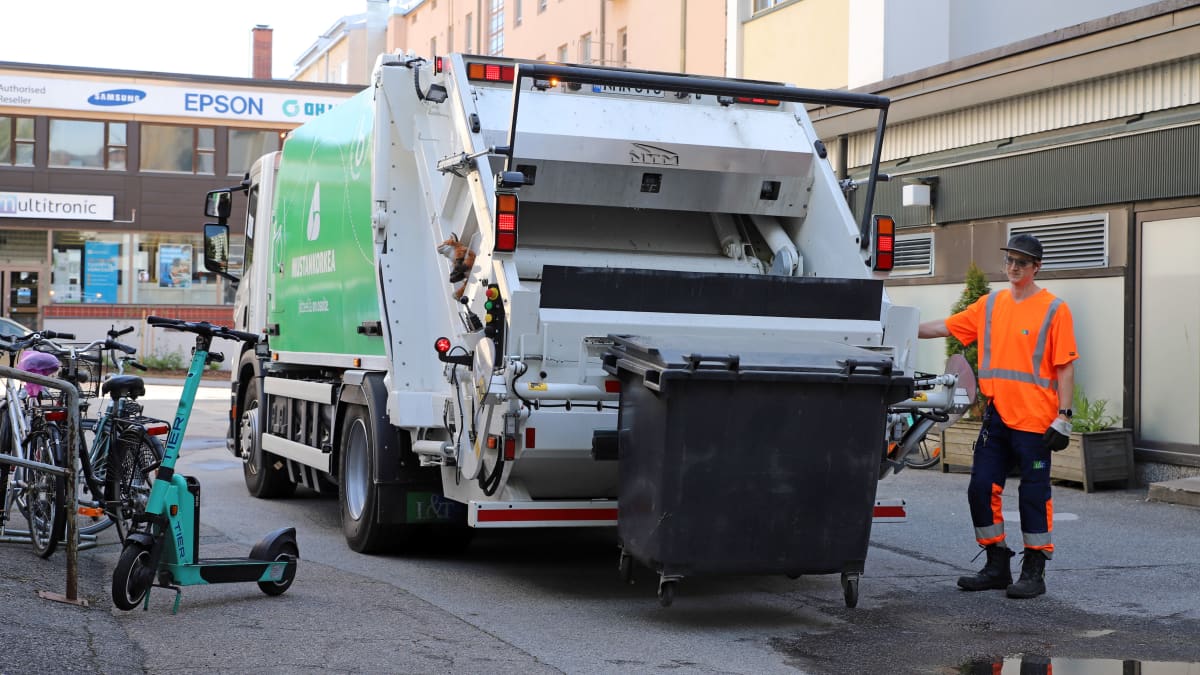 Jäteautonkuljettaja Tuure Vanhanen tyhjentää roskalaatikkoa jäteautoon Jyväskylässä, sähköpotkulauta auton vieressä.