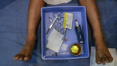 Potilas makaa vuoteella. Potilaan jalkojen välistä löytyy laatikko missä on leikkaukseen tarvittavia työkaluja.