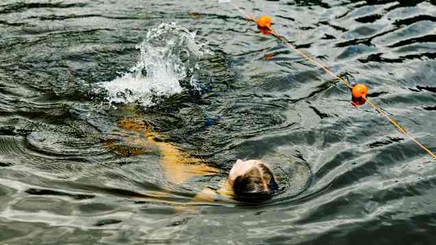 En person simmar ryggsim i en sjö och skapar en liten våg med sina rörelser.