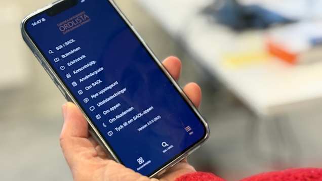 En hand håller i en telefon med Svenska Akademiens ordlista som app öppen.