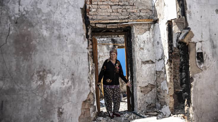 Nainen seisoo pommitusten tuhoaman talon oven suussa.