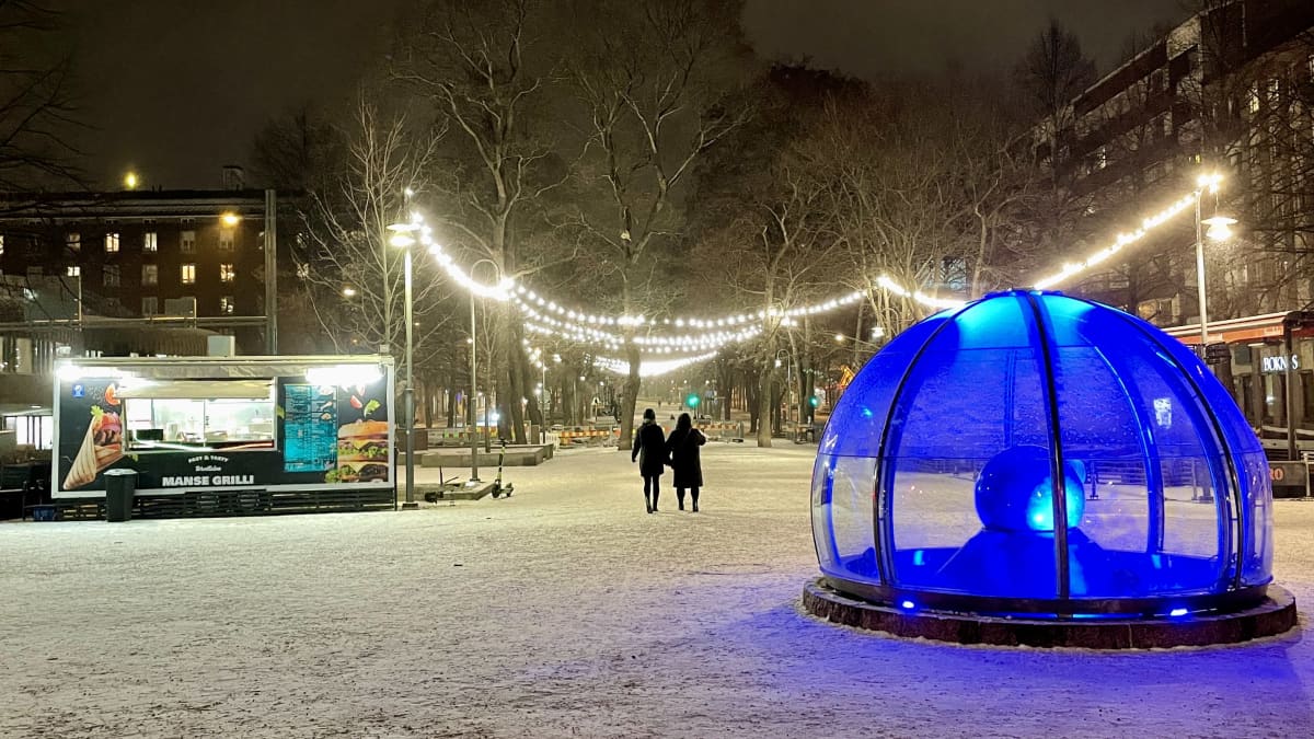 Kaksi tummaa hahmoa kävelee valaistussa talvisessa Hämeenpuistossa.