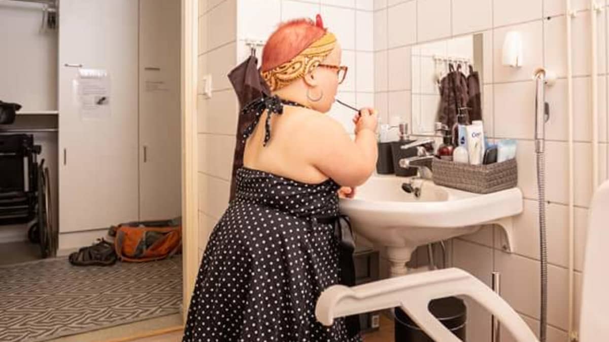 Lyhytkasvuinen Elina Kurvi pesee hampaitaan vessassa, johon on tehty puinen koroke häntä varten.