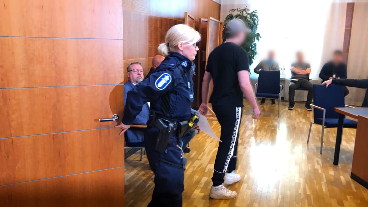 Poliisi tuo murhasta syytettyä uhrin poikaa oikeussaliin Tampereen oikeussalissa.