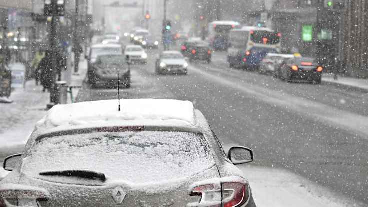 Heavy snowfall on an urban street with pedestrians, cars and a bus.