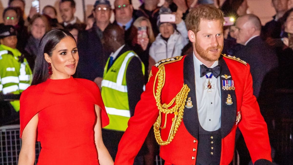 Punaisessa iltapuvussa oleva Meghan ja univormussa oleva Harry pitävät toisiaan kädestä.