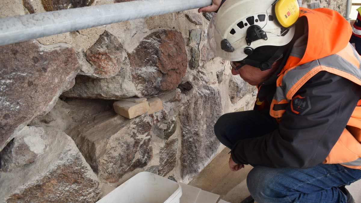 Arkeologi Kari Uotila katsoo muurissa oleva aaukkoa.