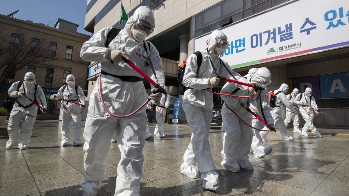 Suoja-asuihin pukeutuneet sotilaat suihkuttavat desinfiointinestettä kadulle Daegussa Etelä-Koreassa 2. maaliskuuta 2020.
