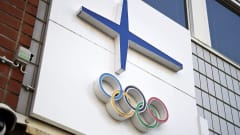 Olympiarenkaat ja Suomen lippua kuvastava sininen risti talon seinässä.