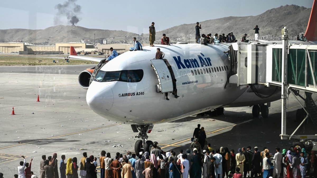 Ihmisjoukko seisoo pysähtyneen lentokoneen päällä Kabulin lentokentällä.