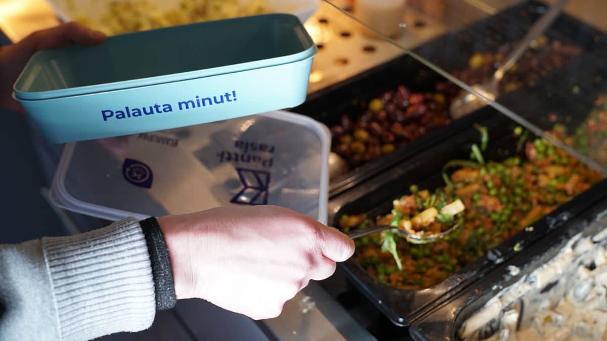 Palautepakkaus kädessä, jota täytetään noutopöydästä.