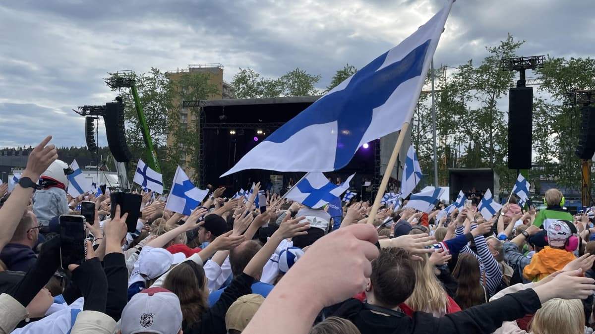 Yleisömeri heiluttamassa Suomen lippuja taivasta vasten.