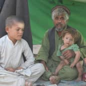 Isä pitää noen likaamaa lastaan sylissa Kabulin pakolaisleirillä. 