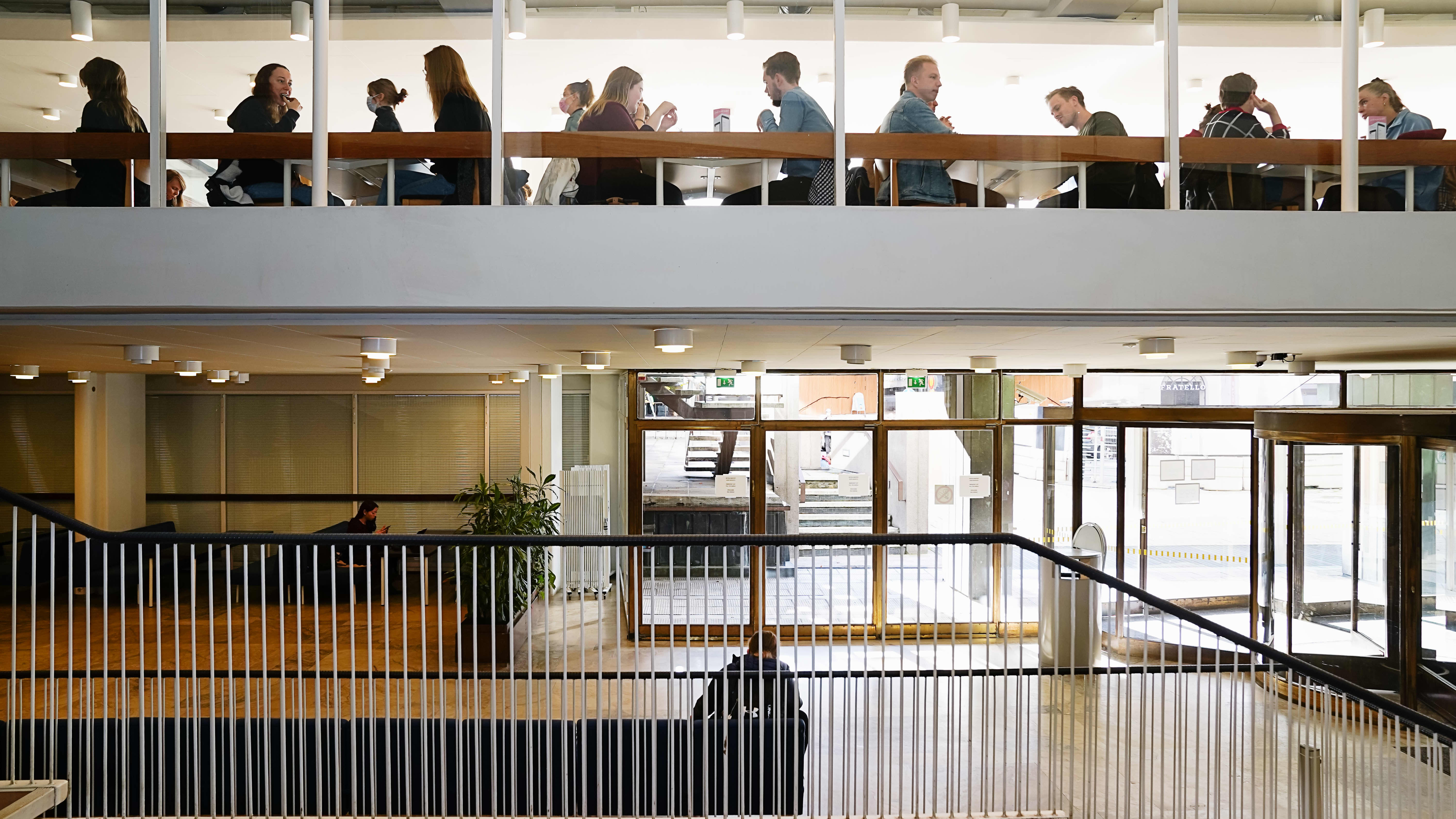 Porthanian aula portailta kuvattuna. ylhäällä näkyy opiskelijoita ruokailemassa opiskelija ravintolassa.