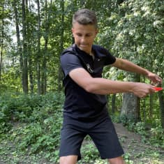Nuori mies heittää frisbeegolfkiekkoa vehreässä metsikössä.