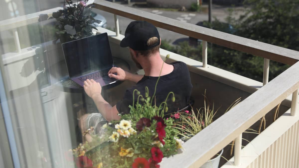Etätyöntekijä työskentelee läppärin ääressä parvekkeella aurinkoisena kesäpäivänä Helsingissä 18. kesäkuuta 2021.