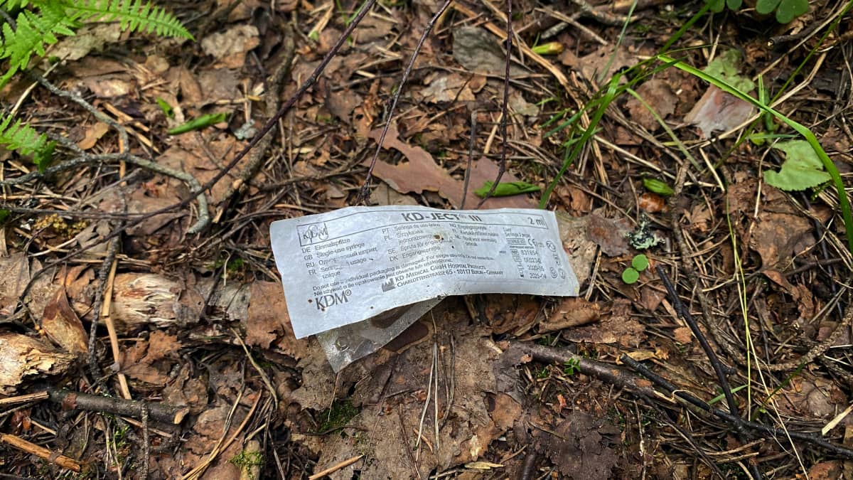 Injektioneulan muovikääre maassa metsässä.
