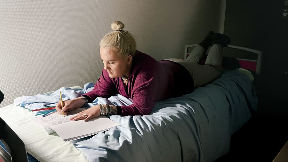 Tanja Heikka värittää aikuisten värityskirjaa psykiatrisen sairaalan potilashuoneessa.