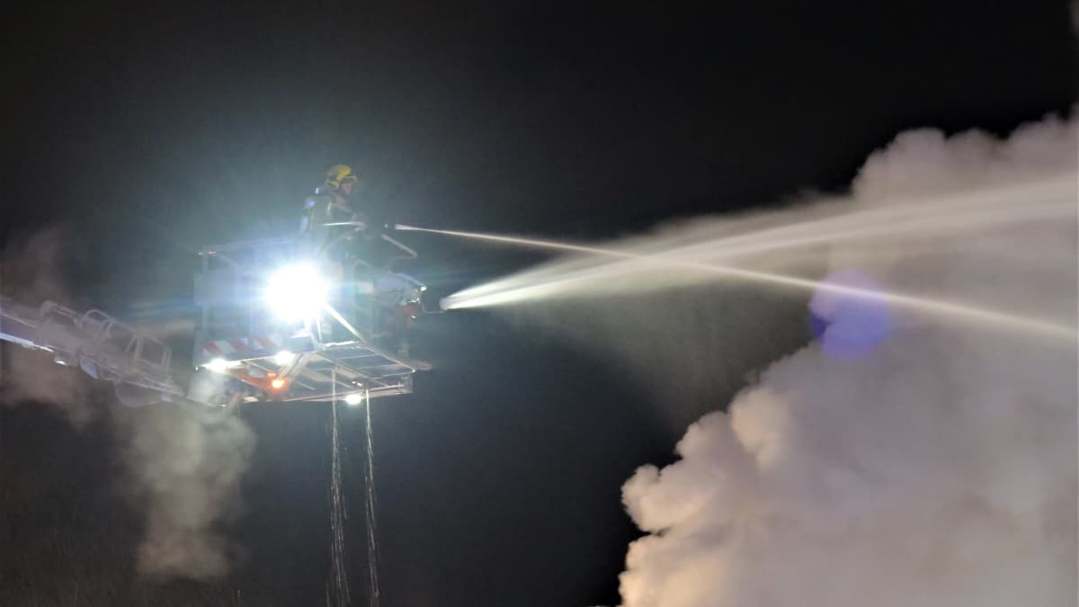 Palomies ruiskuttaa yöllä vettä nosturin korista käsin kohti savupilveä. 