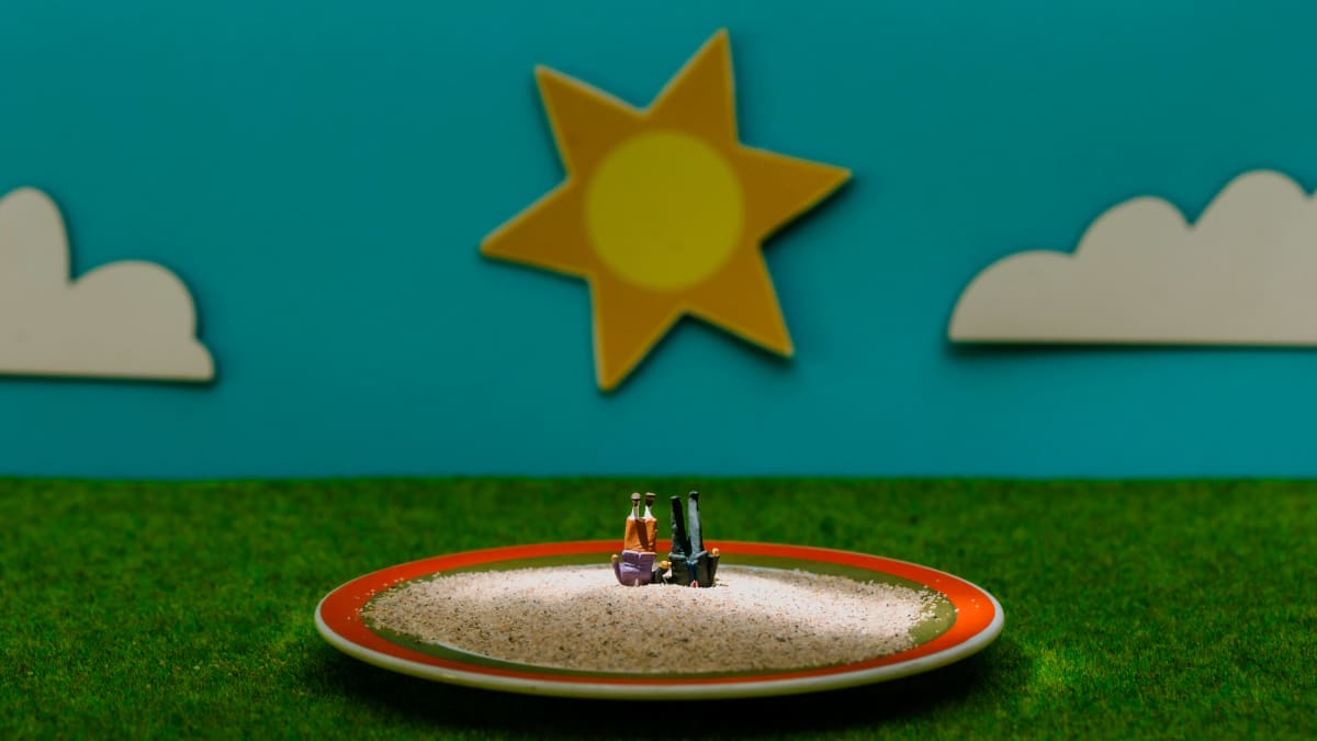 Miniatyyrimaisemassa aurinko paistaa, pienellä lautasella on hiekka jossa kaksi hahmoa seisoo päällään.