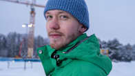 A man looks into the camera against the backdrop of a wintry landscape. 