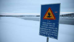 Kyltti Rovaniemellä, joka varoittaa heikosta jäistä. Taustalla osittain sula joki.
