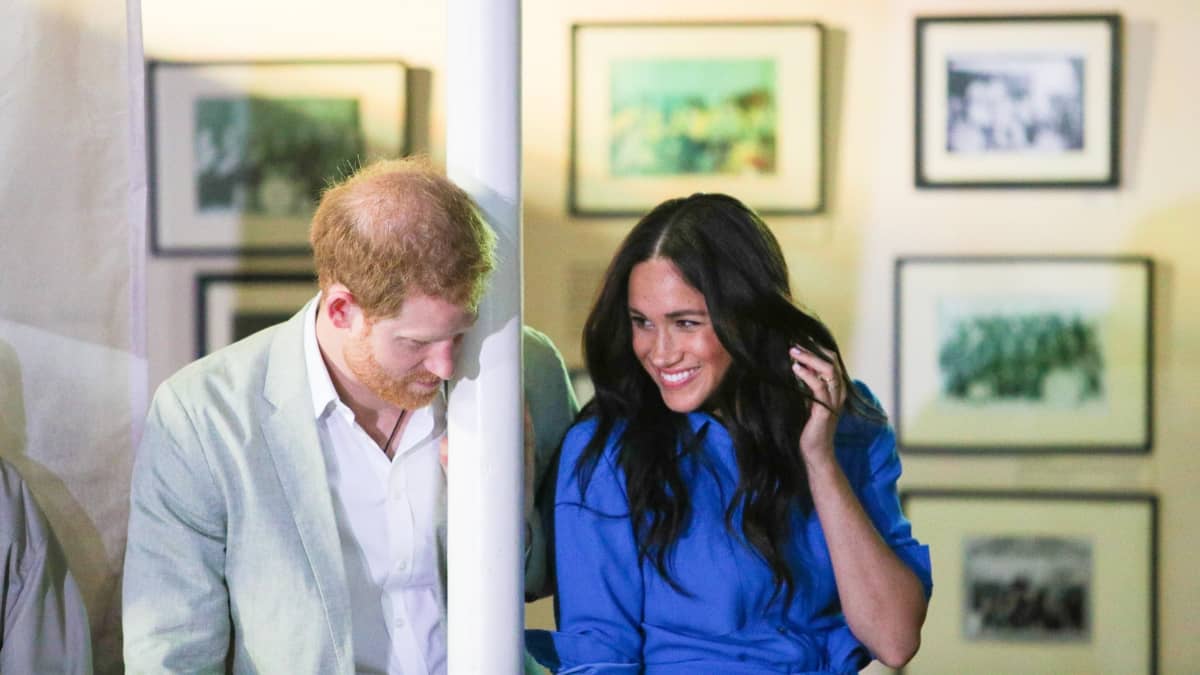 Pylvääseen nojaava prinssi Harry ja hymyilevä Meghan.