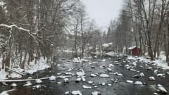 Lumi koristaa Partakosken kiviä, joki virtaa mustavalkoisessa maisemassa.