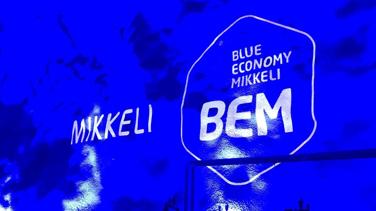 Betoniruiskutetun luolan seinä on valaistu sinisellä värillä ja siihen heijastettu Mikkelin kaupungin ja BEM-osaamiskeskuksen logot.
