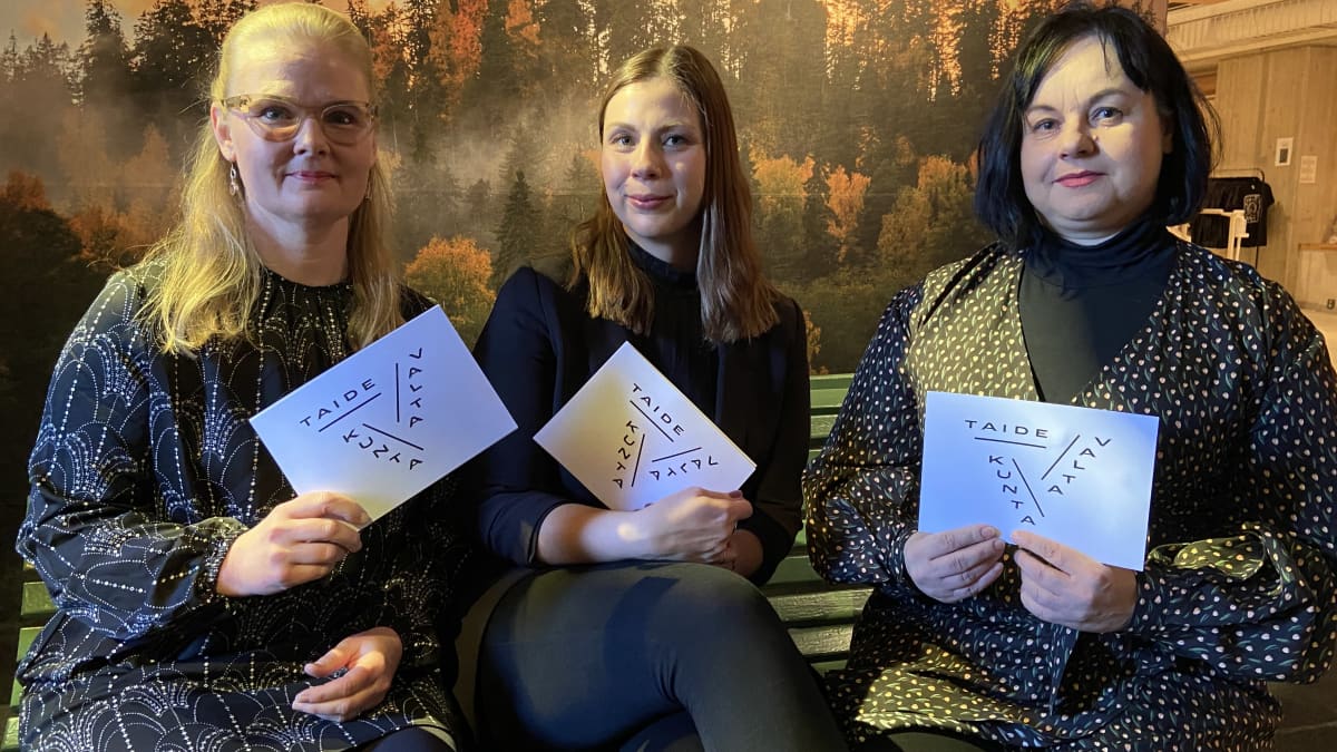 Kolme naista istuu valkoiset papariarkit käsissä.