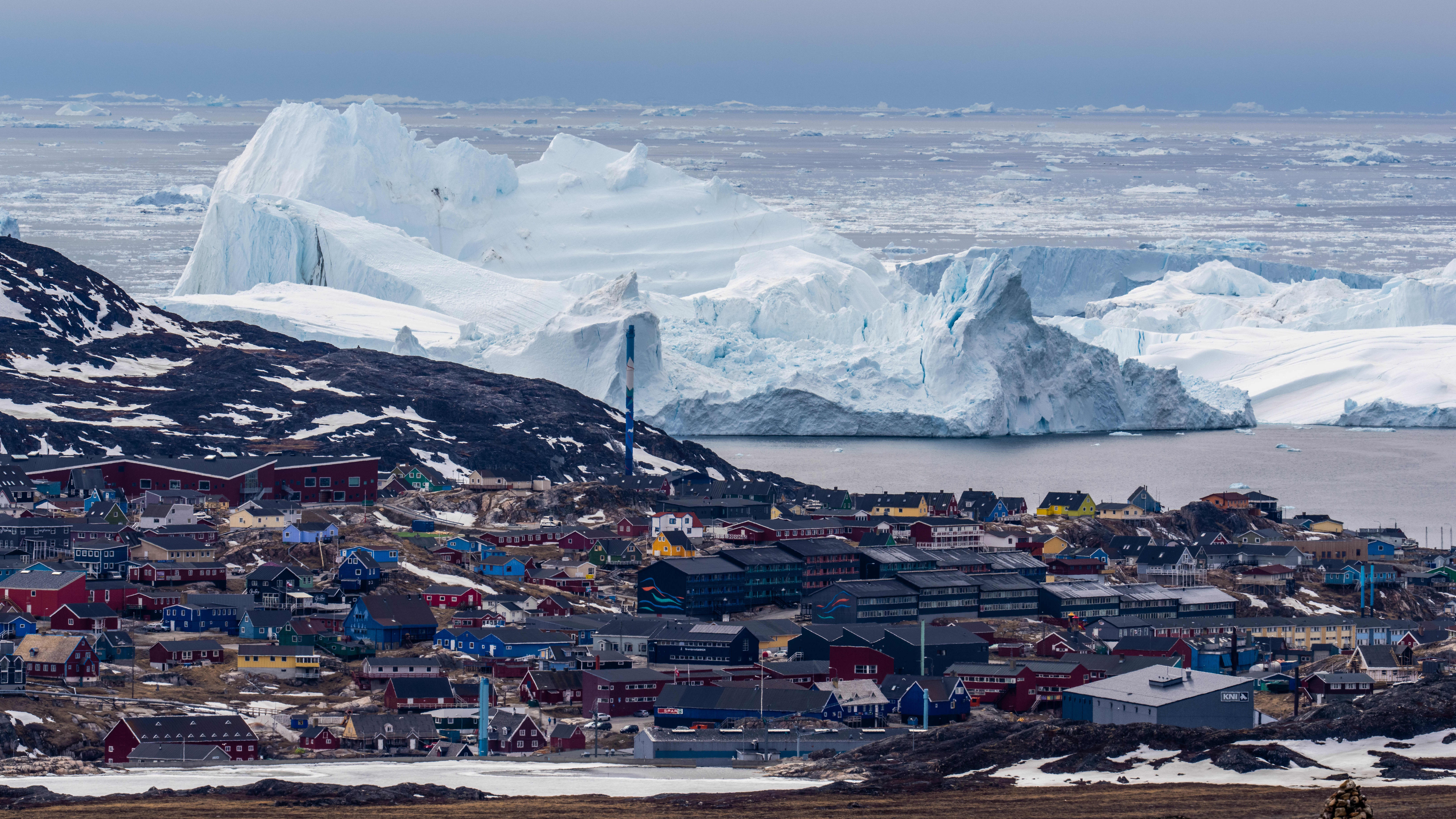 Ilmakuvassa näkyy grönlantilainen rannikkokylä sekä sen takana jäätikköä.