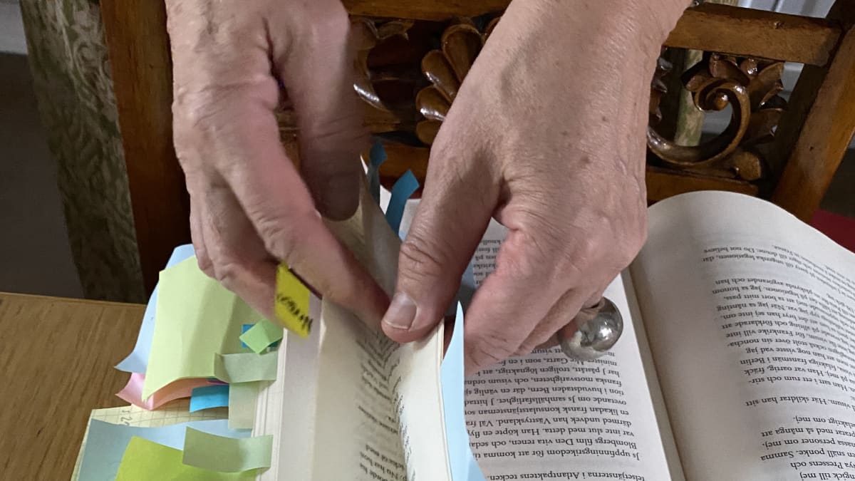 Händer som bläddrar i en bok med post-it-lappar.