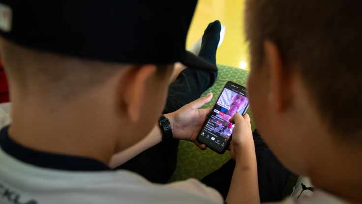 Ala-asteikäisen pojan kädet pitelemässä älypuhelinta, jossa pyörii Tiktok-video. Vieressä kaveri katsomassa samaa ruutua.