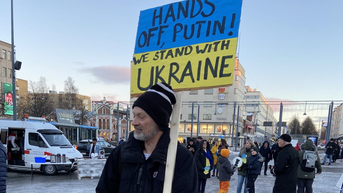 Mies ja sotatoimia vastustava kyltti Vaasan mielenilmauksessa. Kyltissä teksti "Hands off Putin. We stand with Ukraine"