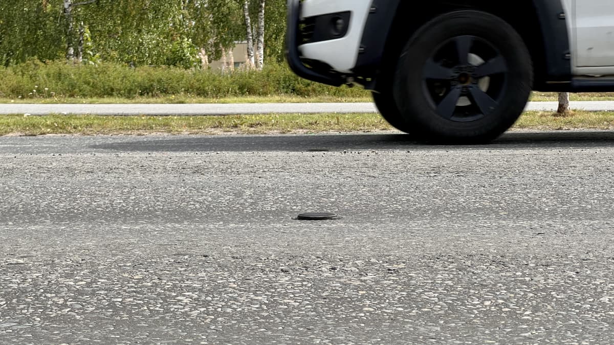 Auto ajaa tiellä, johon on kiinnitetty muutaman sentin korkea pyörän muotoinen täplä. 