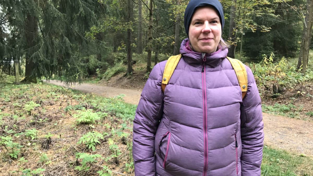 Tutkija Miinu Mäkelä seisoo metsän keskellä Tampereen Kalevanharjulla. Mäkelällä on tummansininen pipo ja lila kevyttoppatakki.