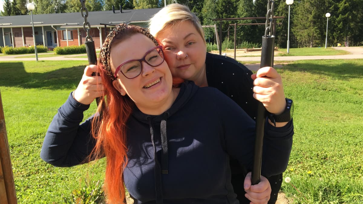 Jenni Hannula istuu keinussa ja Annika Pehkonen seisoo hänen vierellään.