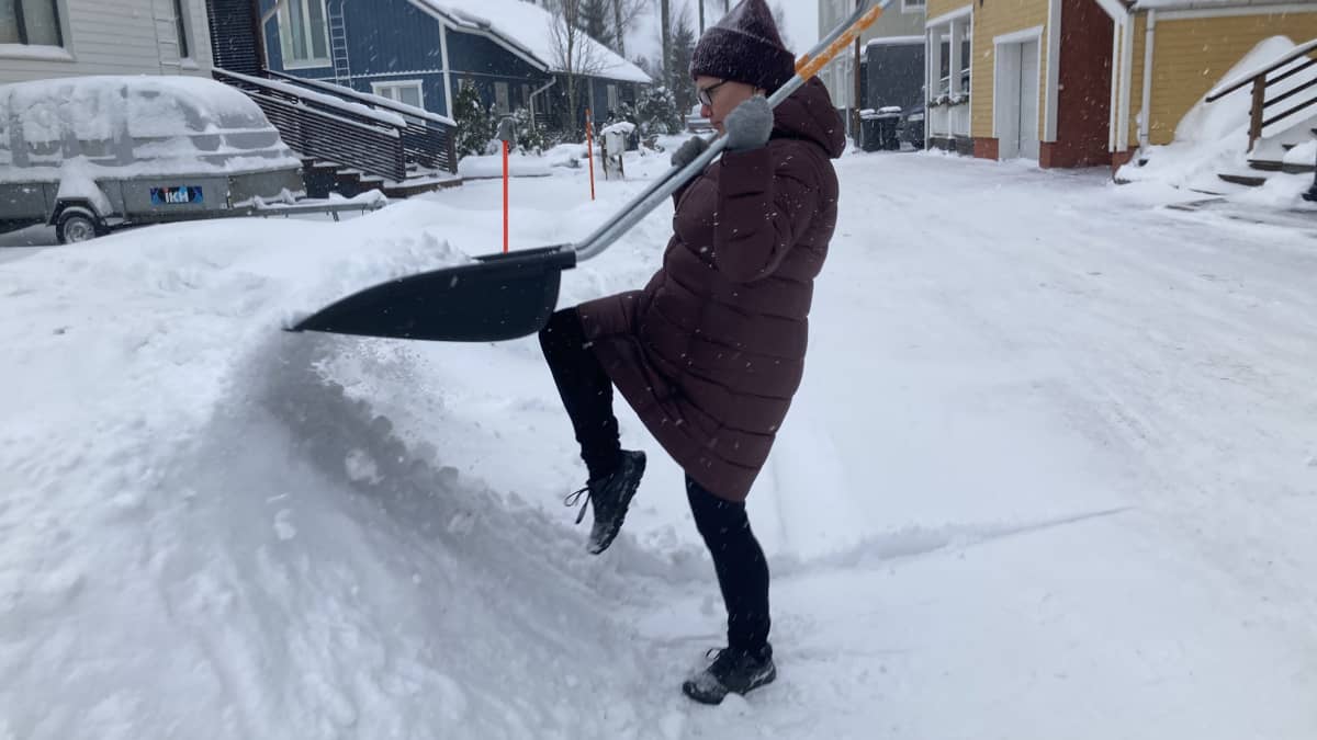 nainen siirtää lumikolalla lunta lumikasaan
