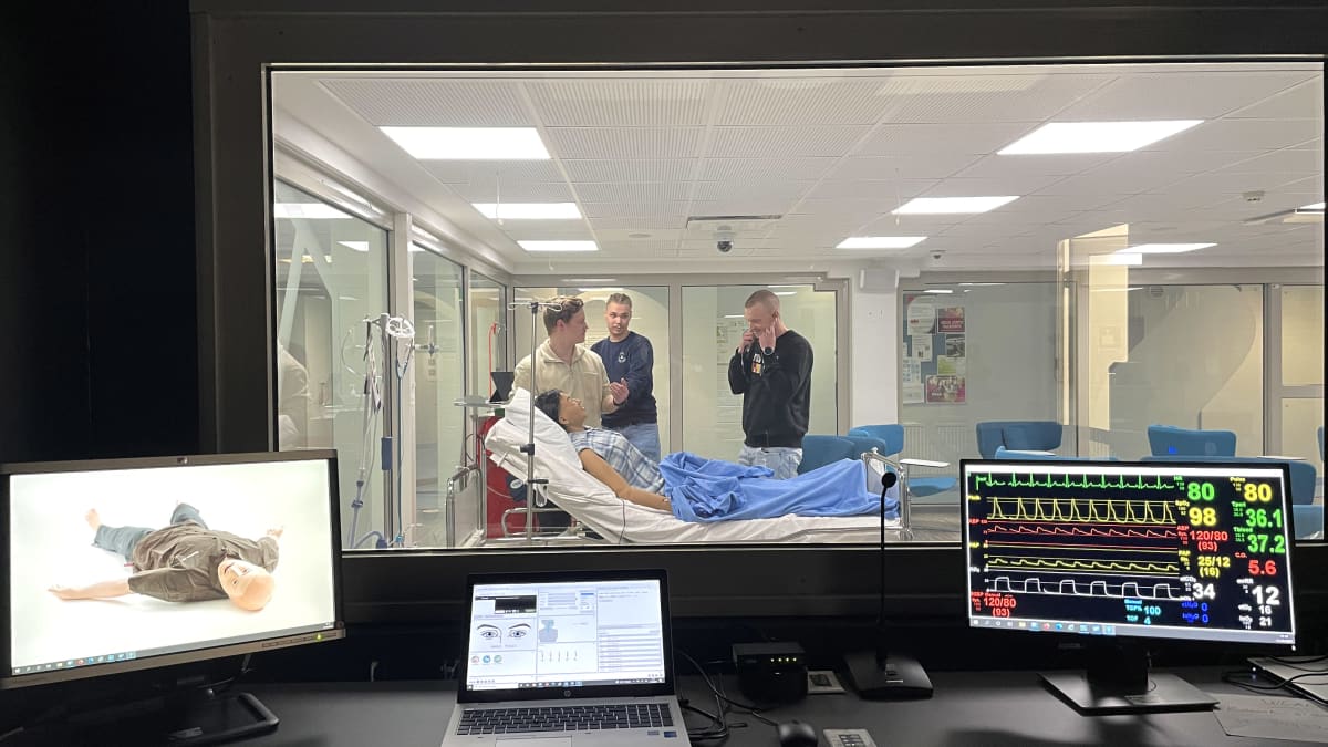 Kolme Kajaanin ammattikorkeakoulussa sairaanhoitajaksi opiskelevaa nuorta miestä on kuvattu simulaatiostudiosta käsin hoitamassa potilasvuoteella makaavaa hoitonukkea. 