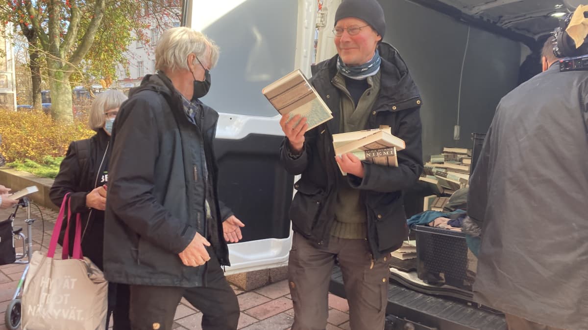 mies jakaa kirjoja pakettiautosta ihmisille